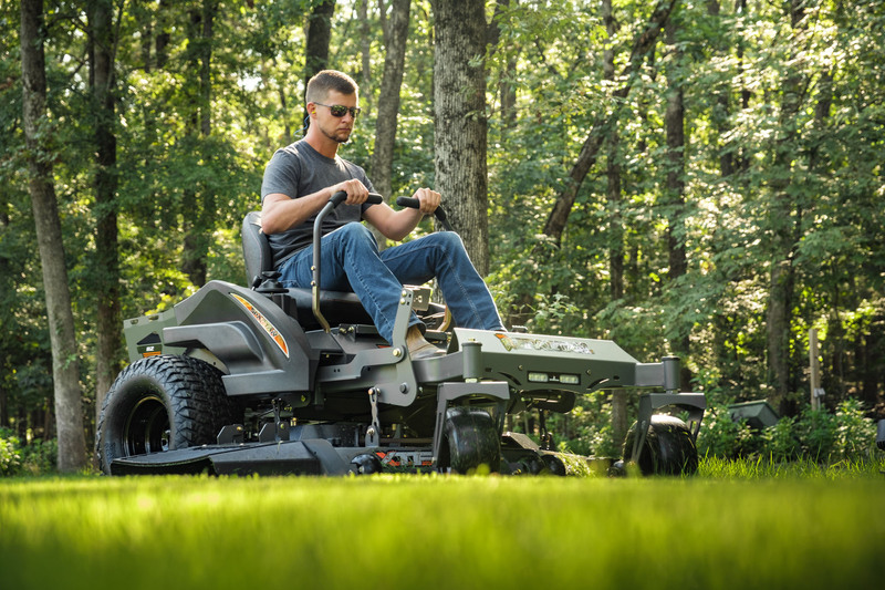 Side view of man riding spartan rz mower with woods in background